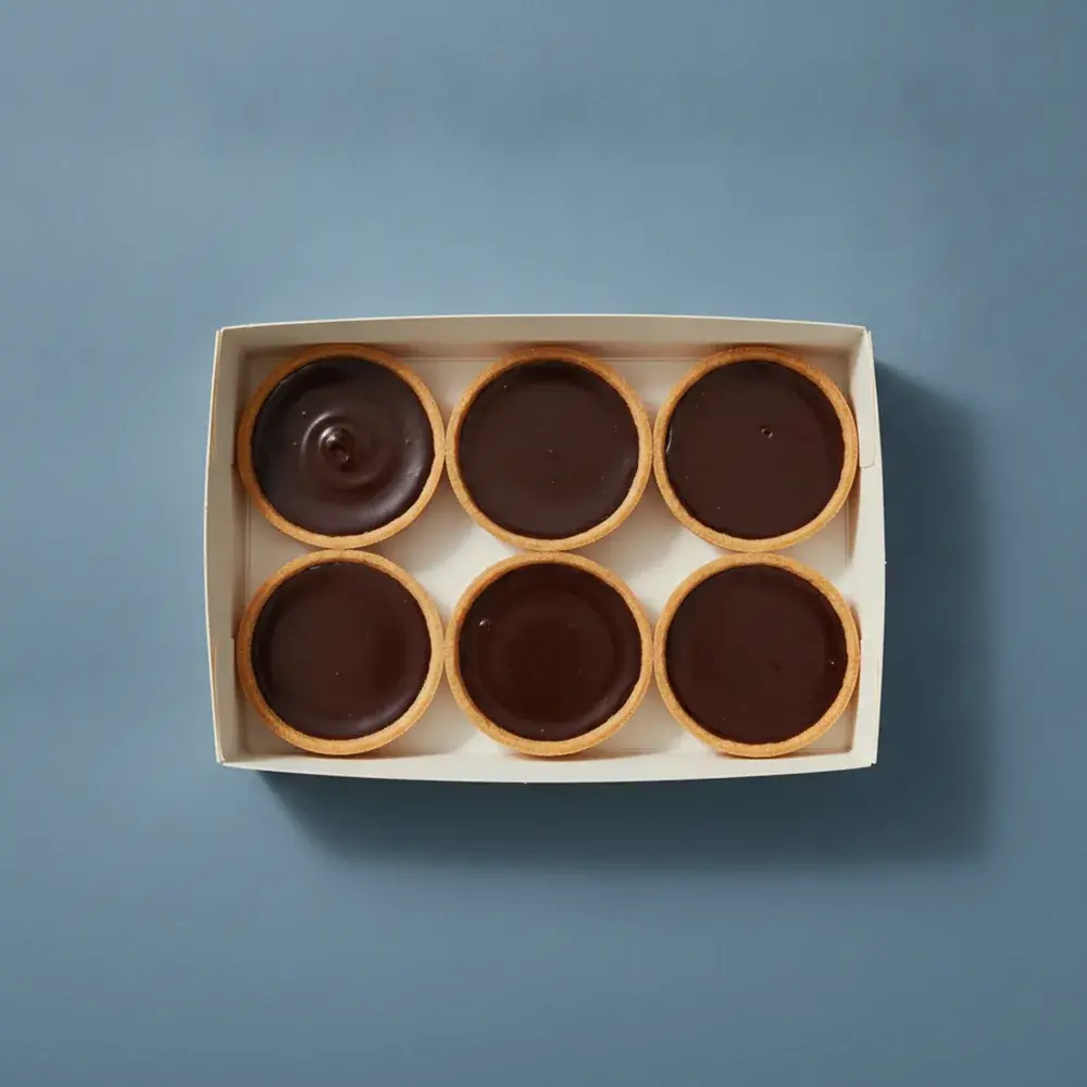 A box of six dark chocolate ganache French tarts, the ganache poured level and set to a mirror