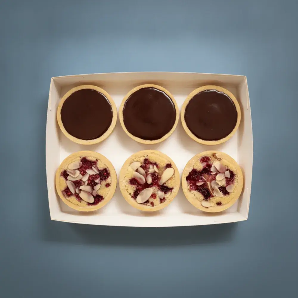 A box of six French tarts split between two flavours, three dark chocolate ganache and three raspberry almond bakewell