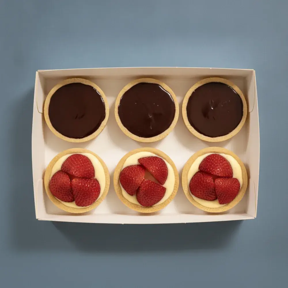 An open box of six French dark chocolate ganache and strawberry custard tarts, seen from above