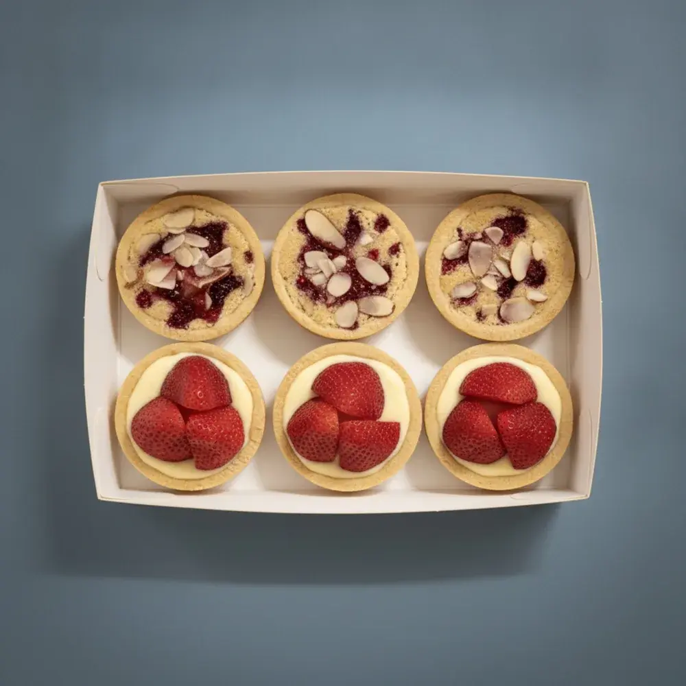 An open box of six French raspberry almond bakewell and strawberry custard tarts, seen from above