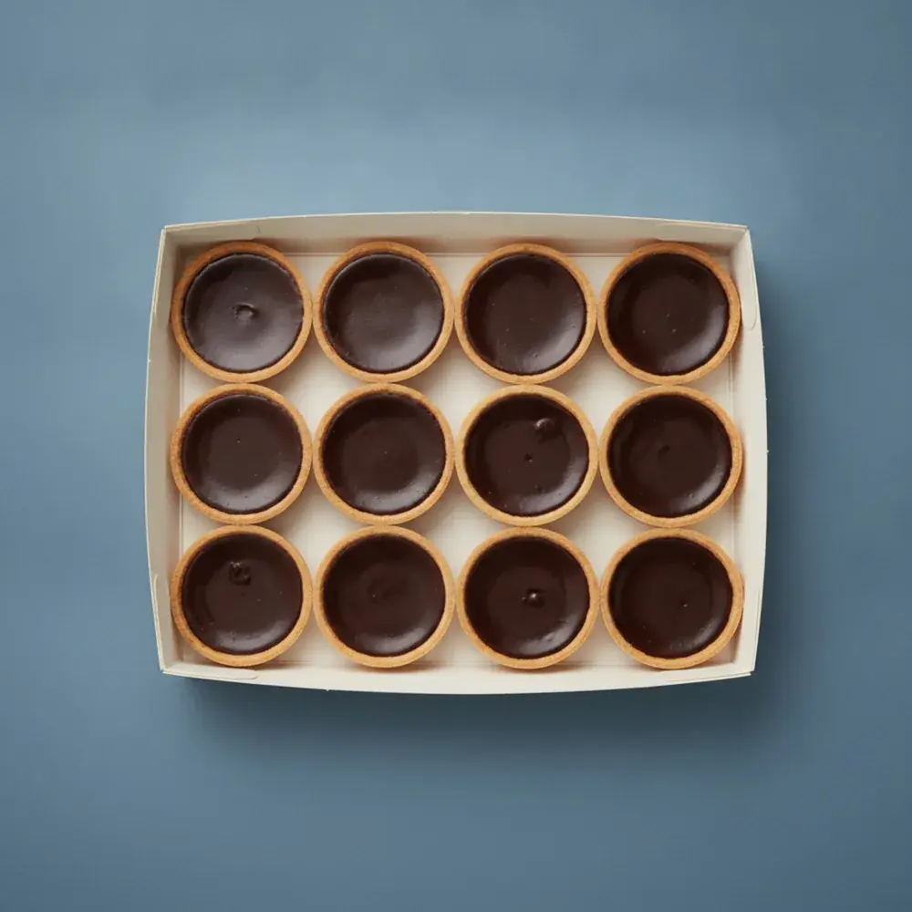 An open box of twelve French dark chocolate ganache tarts, seen from above