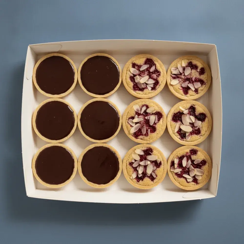 An open box of twelve French dark chocolate ganache and raspberry almond bakewell tarts, seen from above