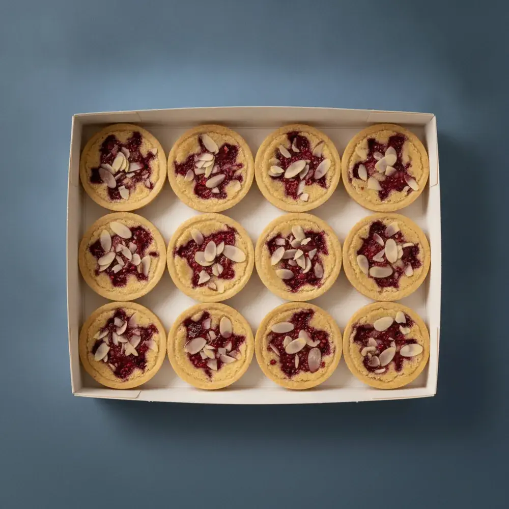 An open box of twelve French raspberry almond bakewell tarts, seen from above